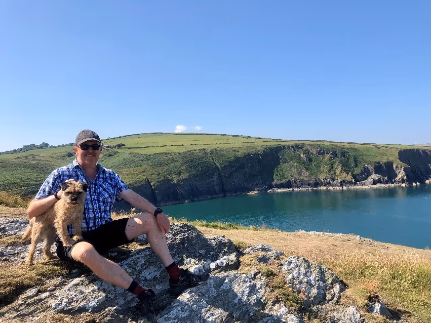 Richard pictured sitting on a rock by a Lake.